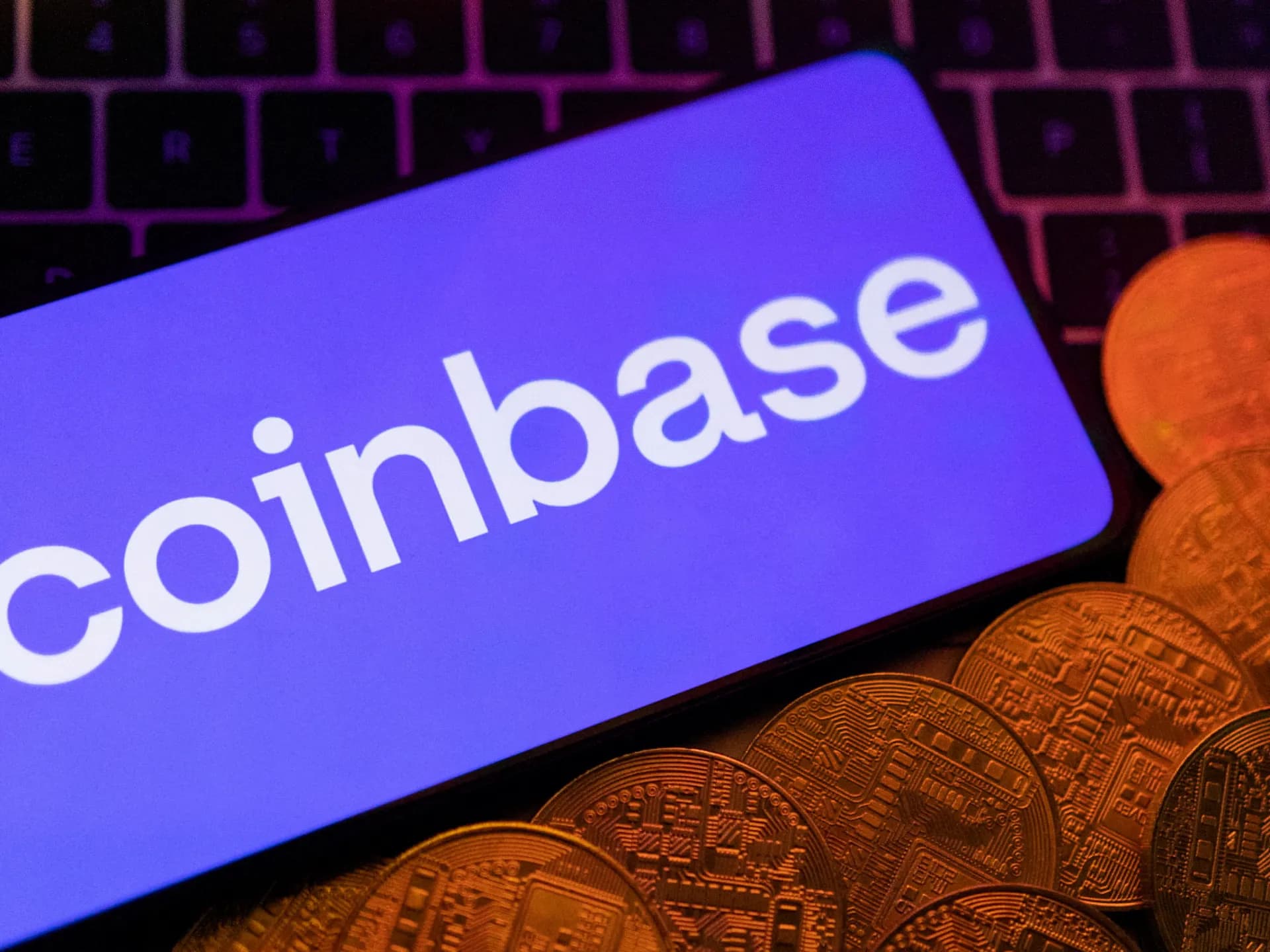 Teléfono con el logotipo de Coinbase junto a representaciones de criptomonedas