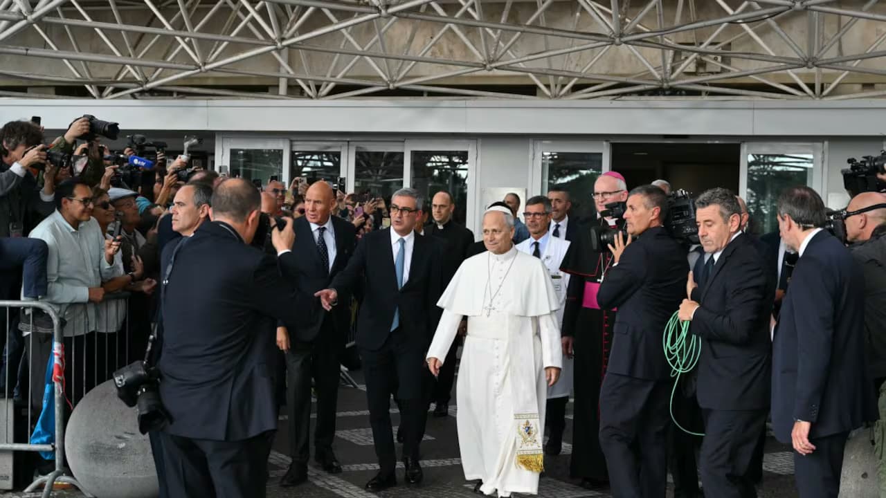 El papa León XIV sale caminando por la entrada principal del hospital Gemelli de Roma, rodeado de fotógrafos y personal de seguridad