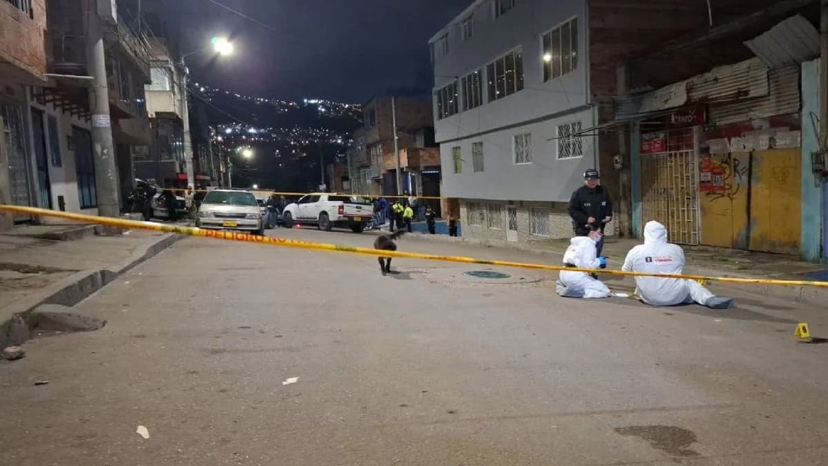 Peritos con trajes blancos trabajan de rodillas sobre el asfalto acordonado con cinta amarilla en una calle empinada del sur de Bogotá, de noche