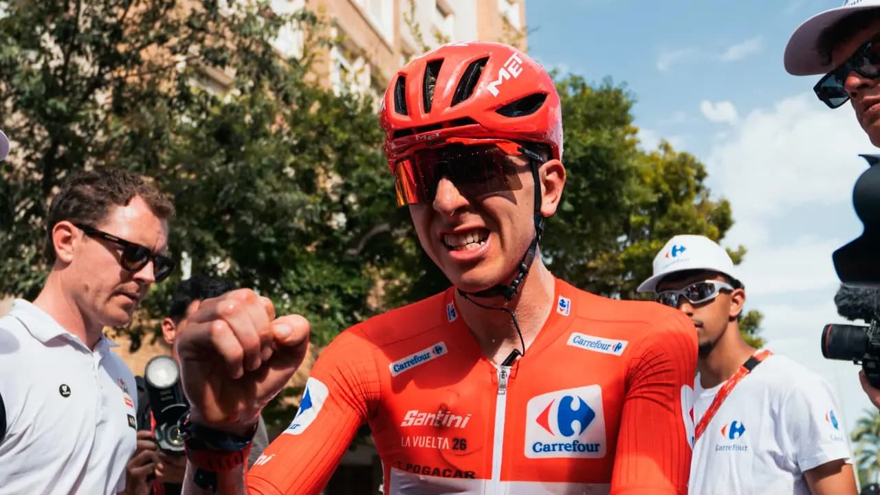 Tadej Pogacar con el maillot rojo de líder y casco rojo, rodeado de personal del equipo tras cruzar la meta