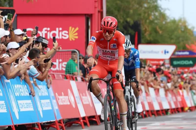 Tadej Pogacar cruza la meta con el maillot rojo de líder mientras el público lo graba con teléfonos desde detrás de las vallas