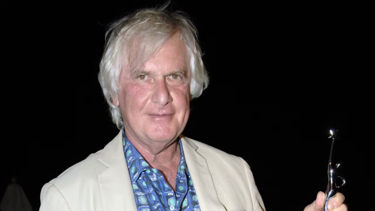El director de cine Peter Medak, de cabello blanco y saco claro, sostiene un trofeo