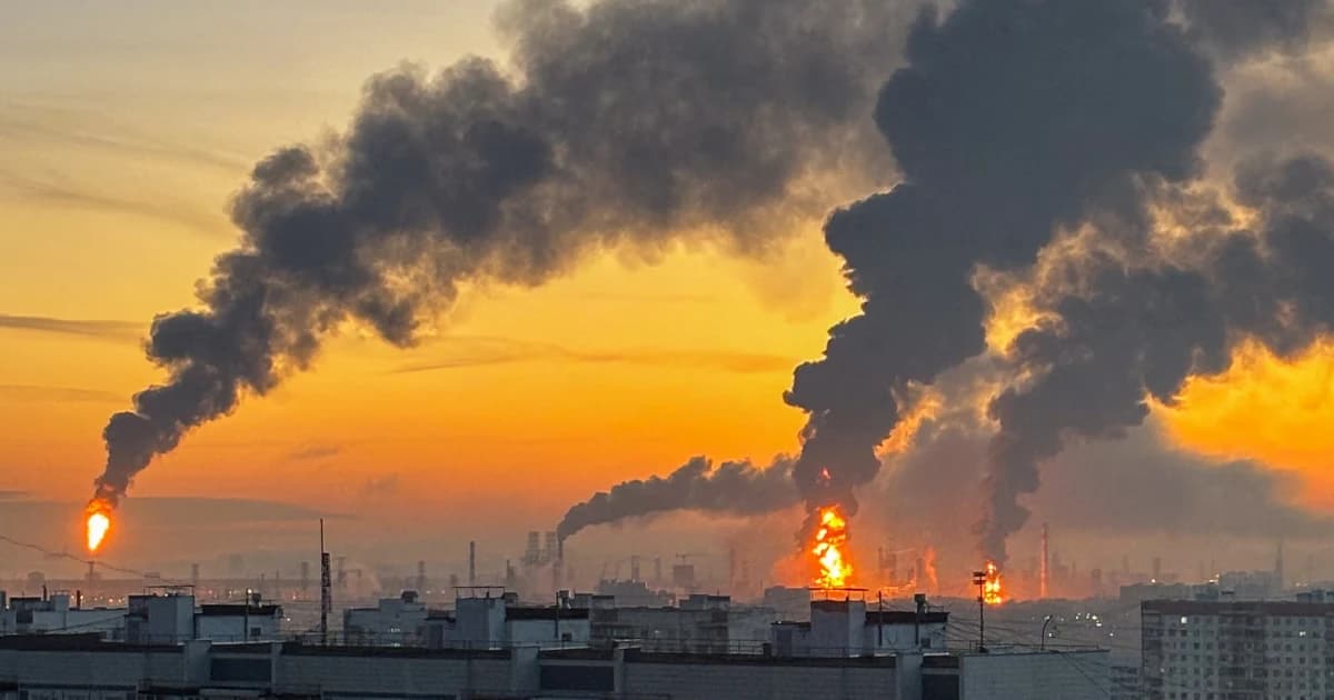 Columnas de humo y llamas se elevan de una refinería al amanecer, con edificios residenciales en primer plano