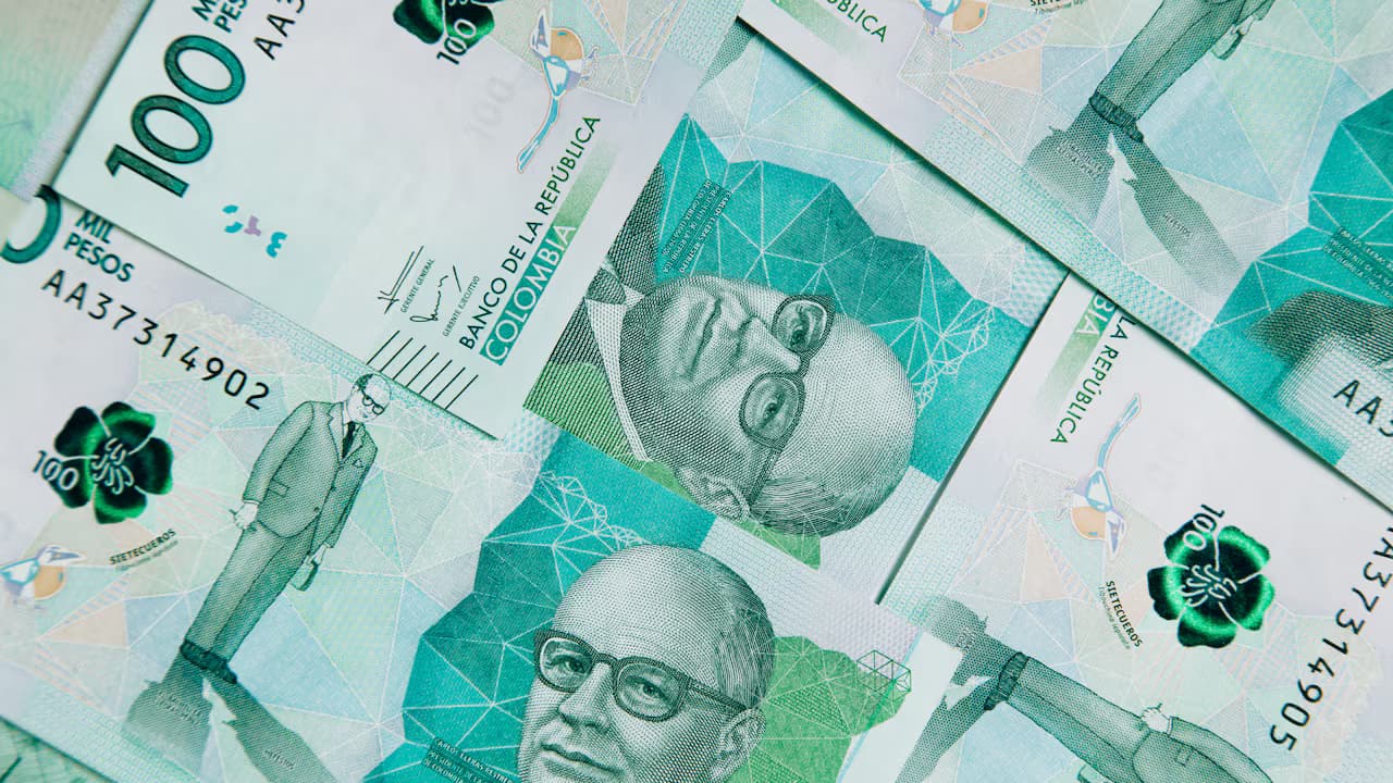 Varios billetes colombianos de cien mil pesos extendidos y superpuestos sobre una superficie plana