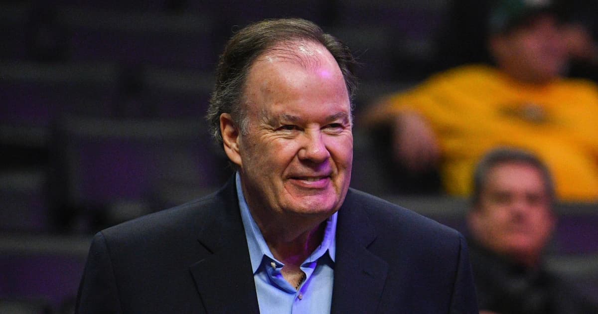 El actor Dennis Haskins, sonriente, con saco oscuro y camisa azul claro, en unas graderías