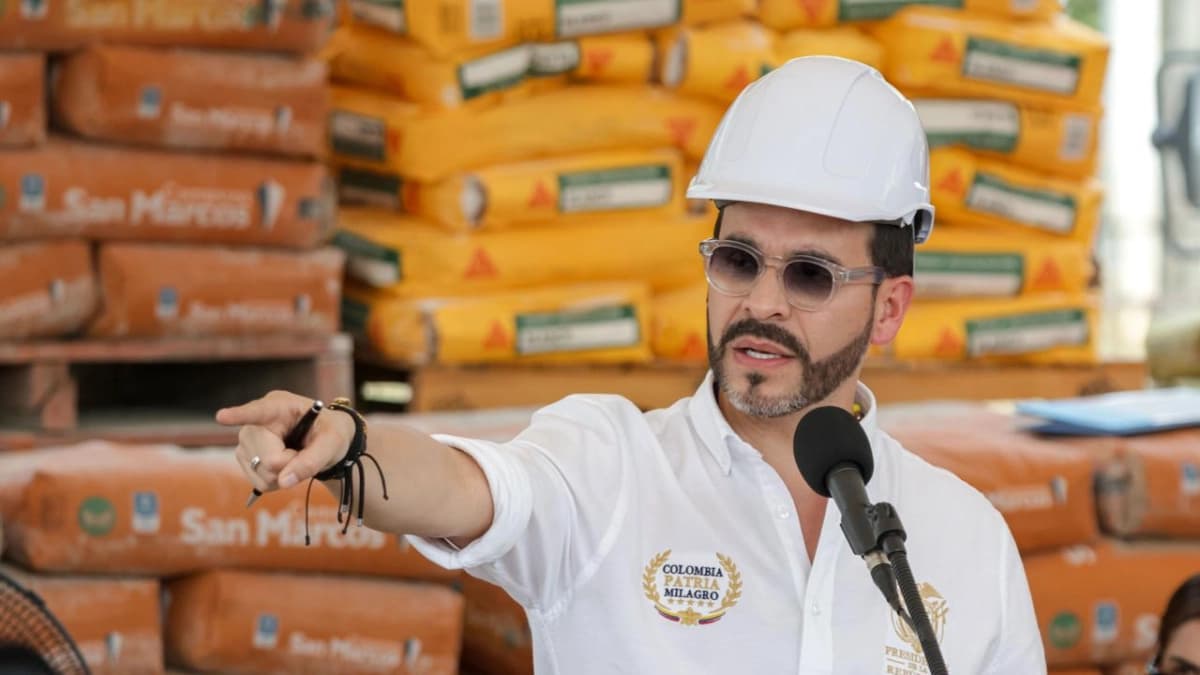 El presidente Abelardo de la Espriella, con casco blanco y gafas oscuras, señala con la mano mientras habla ante un micrófono frente a estibas de bultos de cemento
