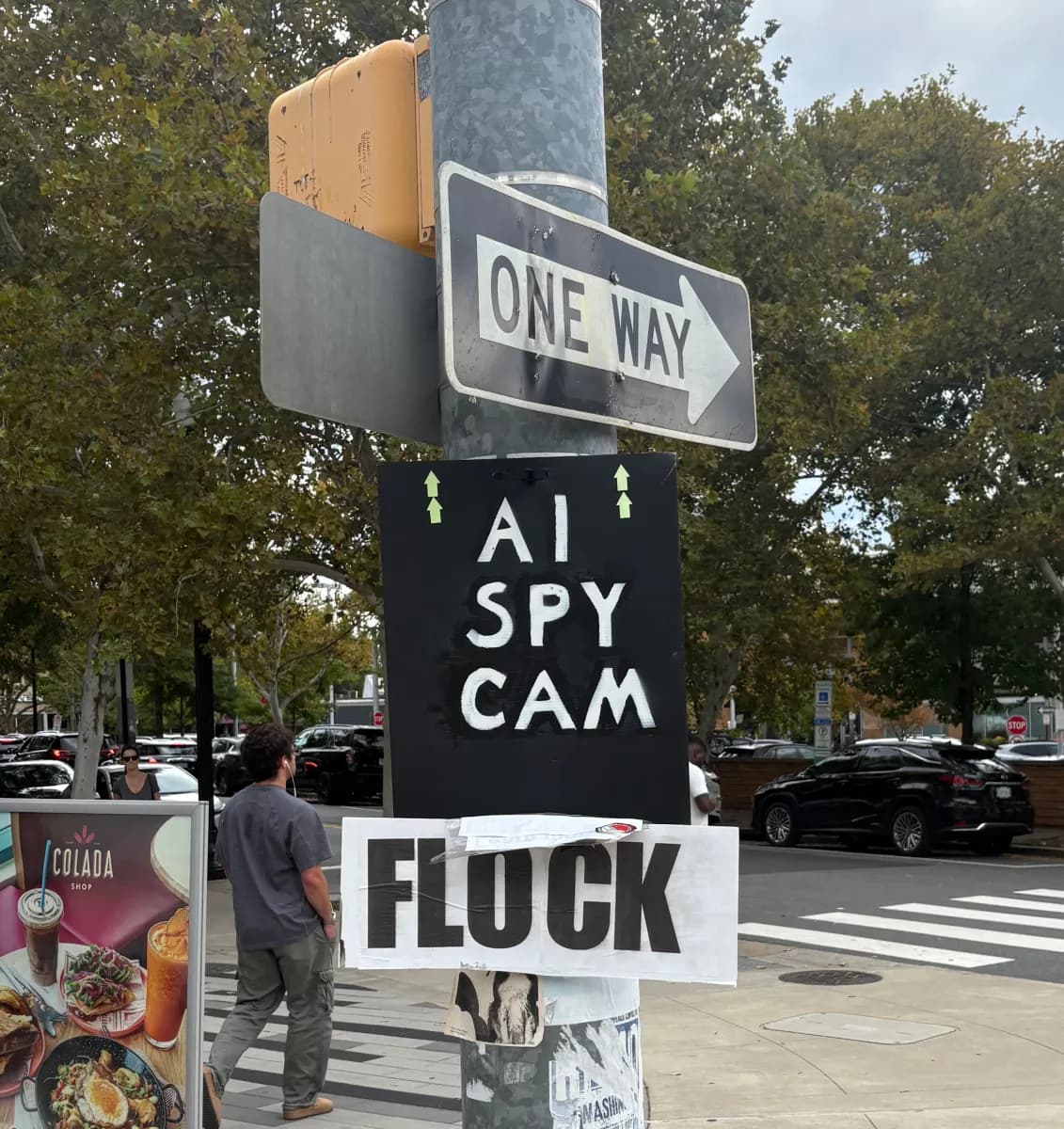Cartel de protesta con las palabras «AI spy cam» y «Flock» pegado a un poste en una calle